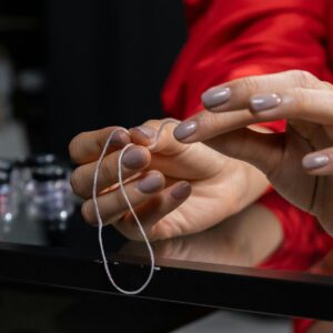 Close-up of manicured hands entwining thread, showcasing nail art and fashion.